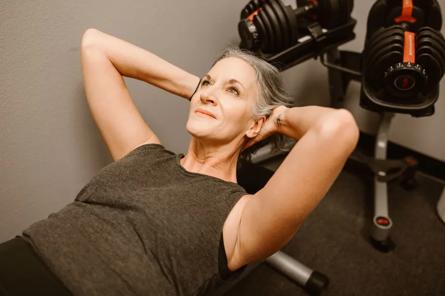 Woman in her fifties with gray hair resting between exercises at a home gym