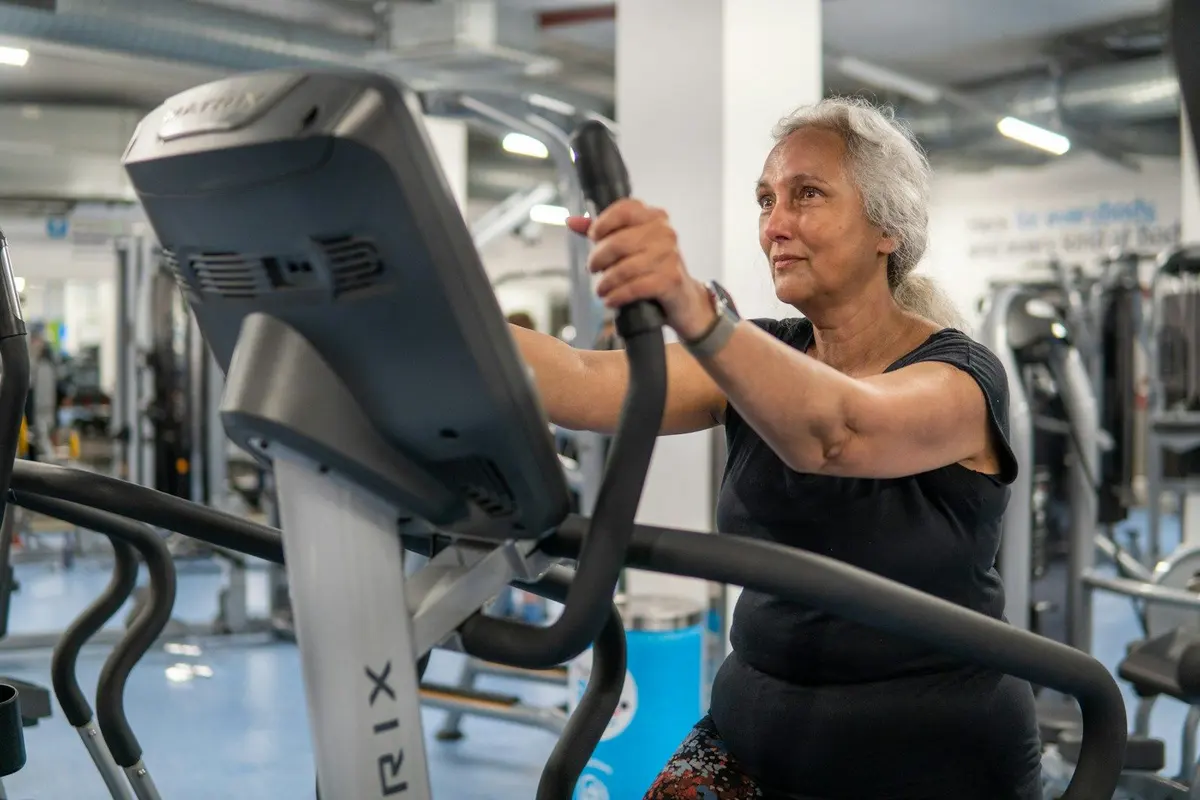Woman in her sixties with gray hair exercising on a cross trainer in a gym