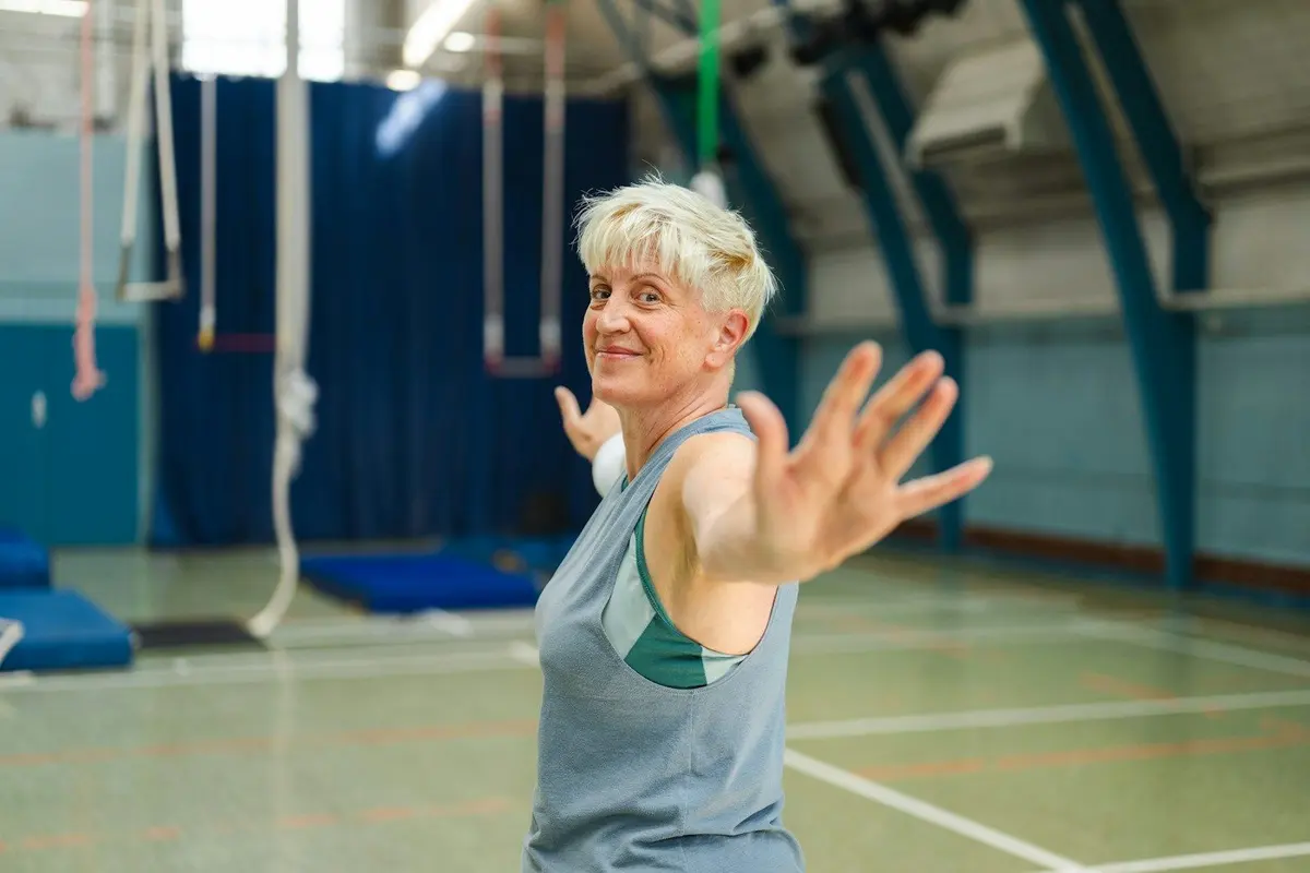 Smiling woman over 50 with short blonde hair stretching her arm during a workout in a gym