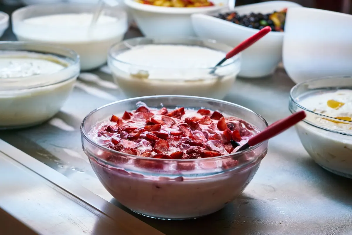 Glass bowl of yogurt topped with red berries next to small bowls of creamy yogurt