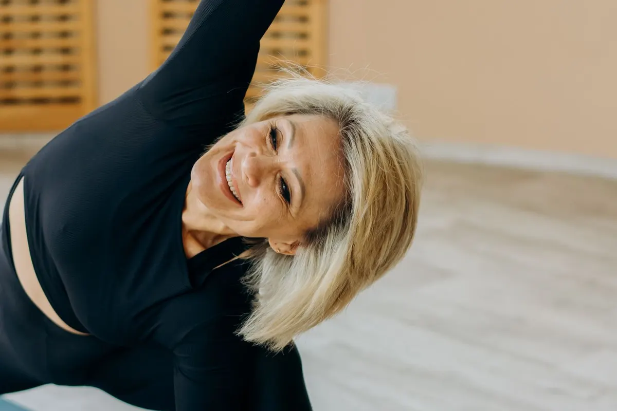 Smiling woman in her 50s stretching to the side on a yoga mat