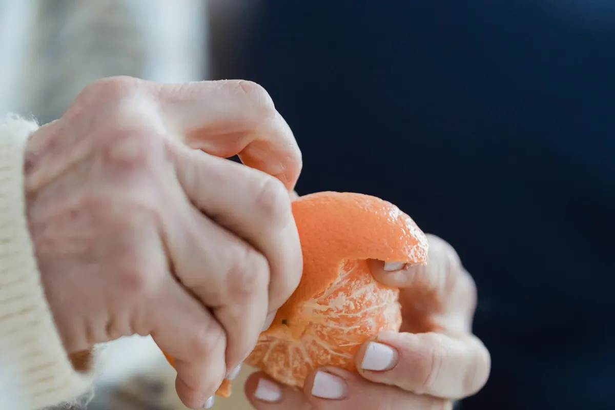 Hands of a woman over 50 peeling a fresh mandarin as a fiber-rich snack