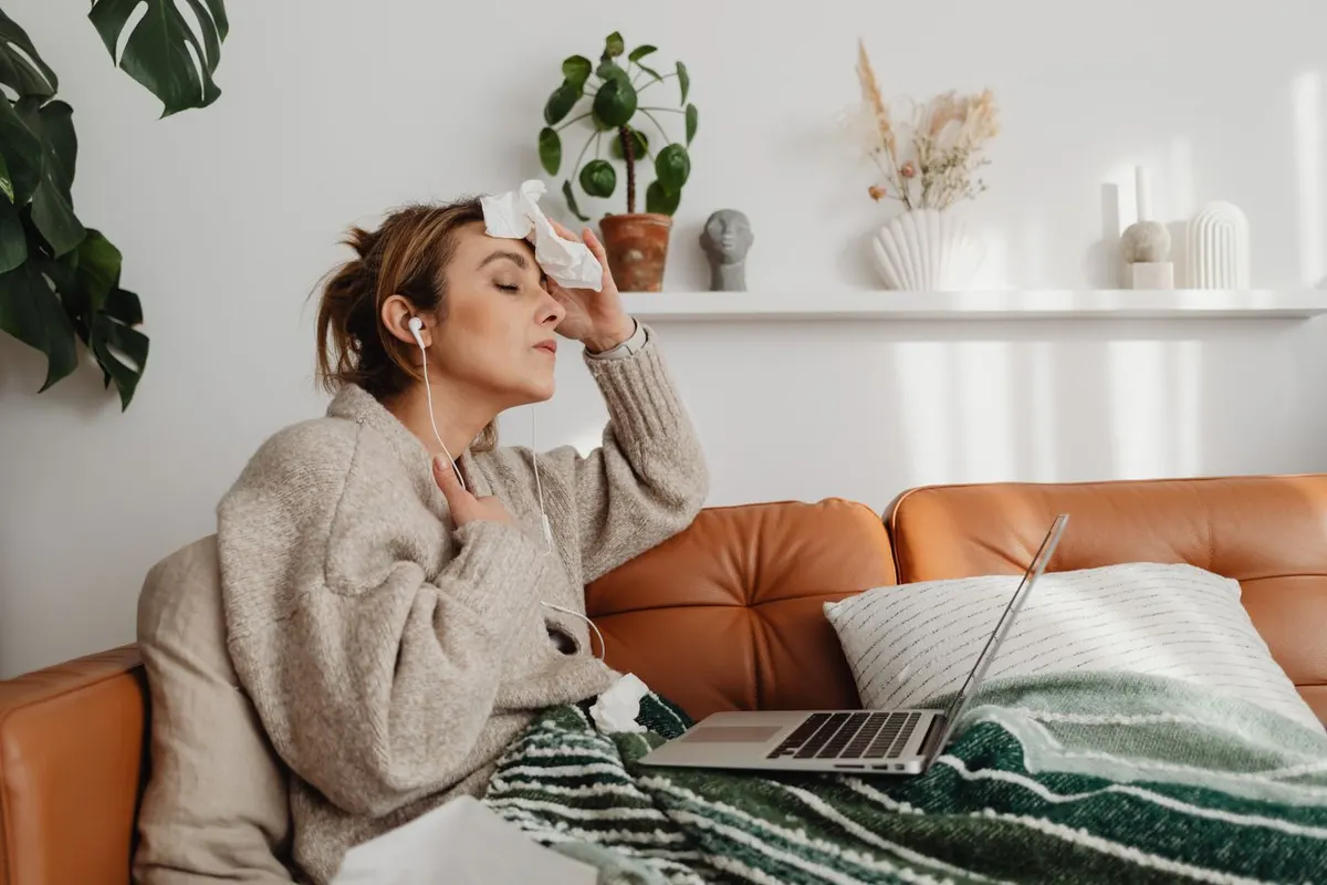 Woman on a couch wiping her forehead with a tissue during a hot flash