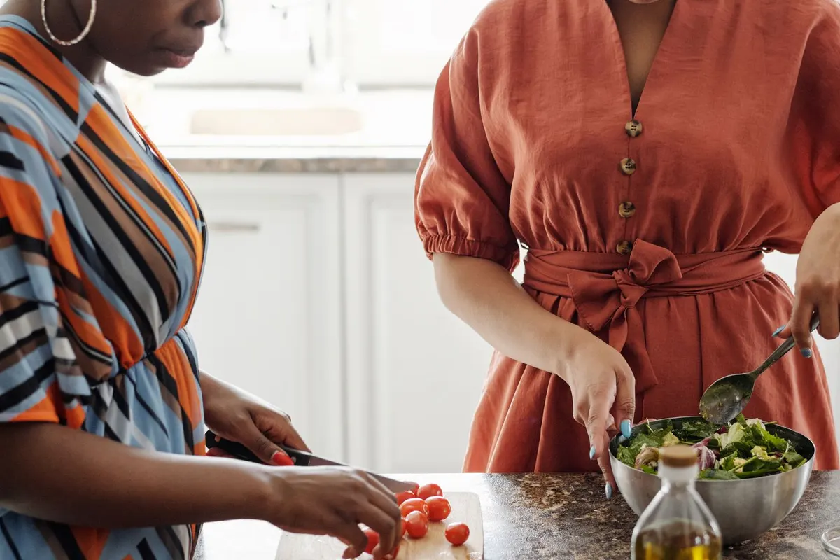 Two women preparing a fresh green salad with tomatoes and olive oil in a home kitchen