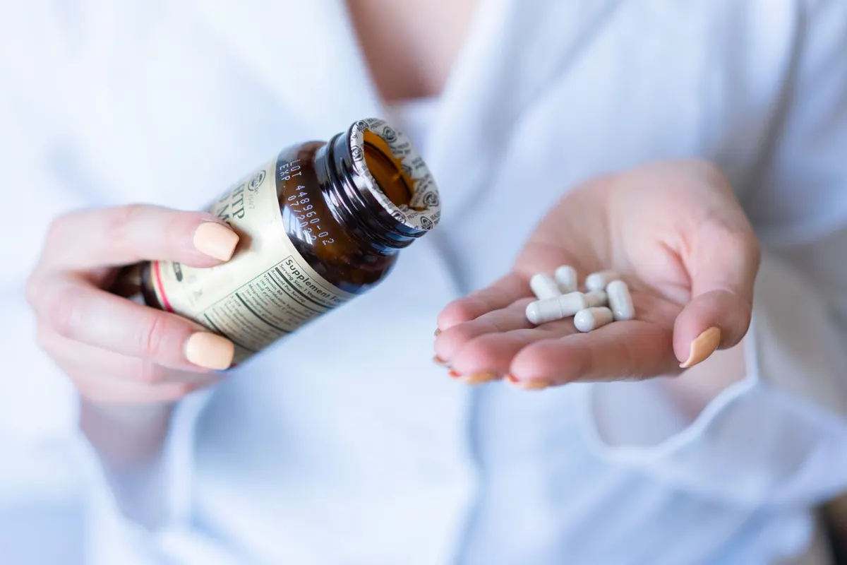 Woman in a white shirt holding a supplement bottle and a few white capsules in her open palm