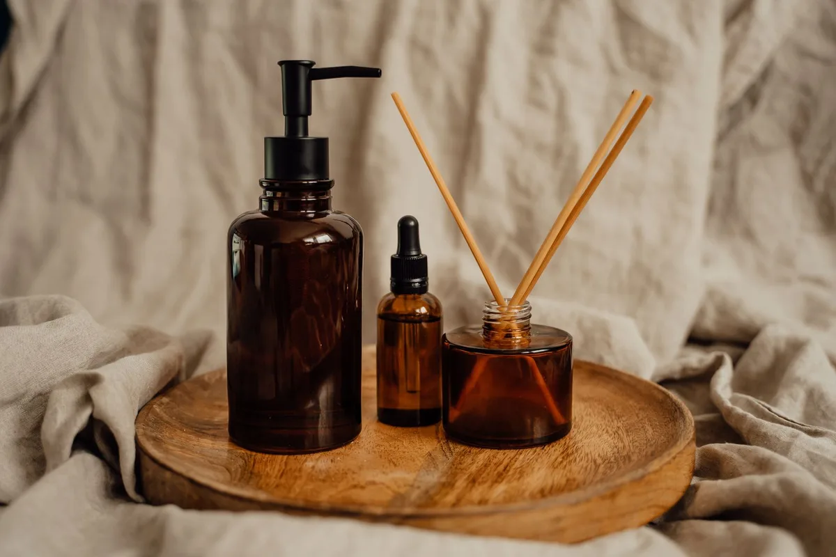 Amber glass self-care bottles and a diffuser arranged on a wooden tray