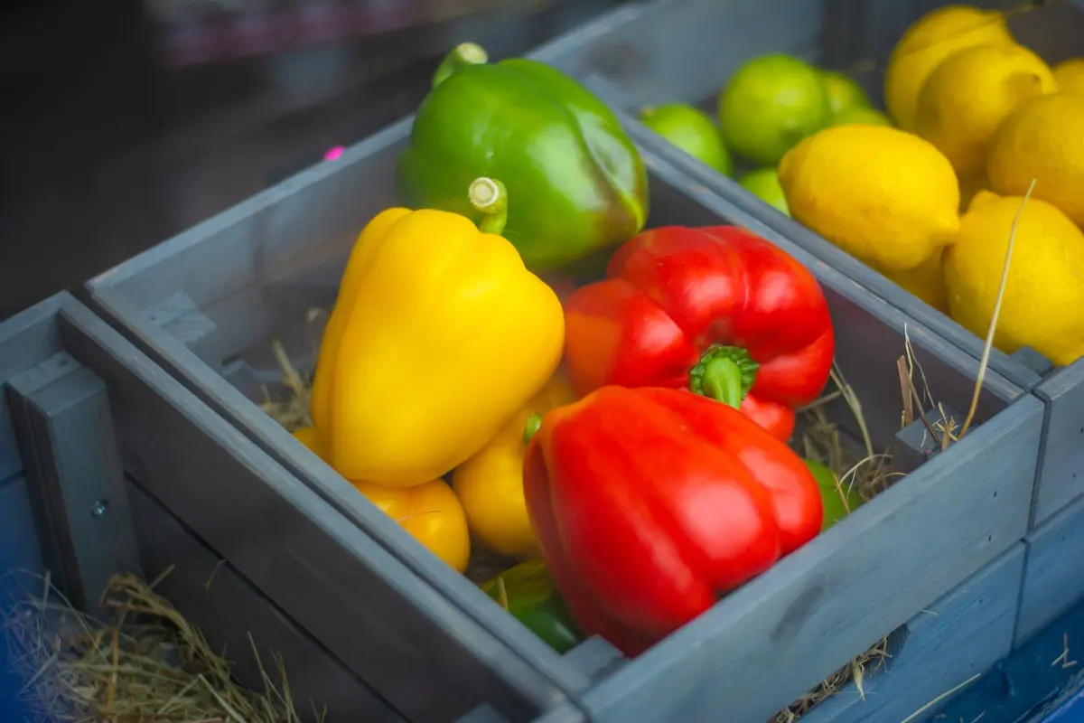 Wooden market crate filled with red, yellow and green bell peppers and fresh lemons
