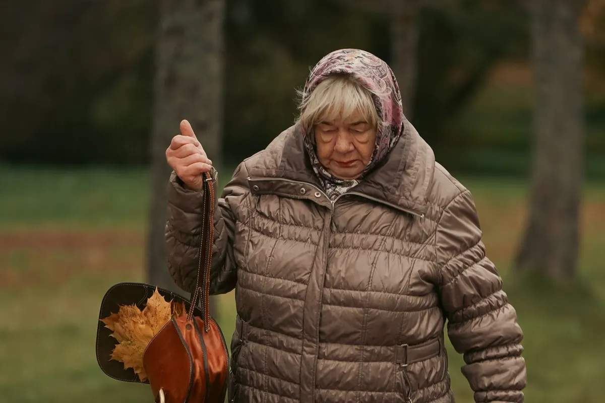 Woman over 50 in a quilted jacket and headscarf walking through an autumn park
