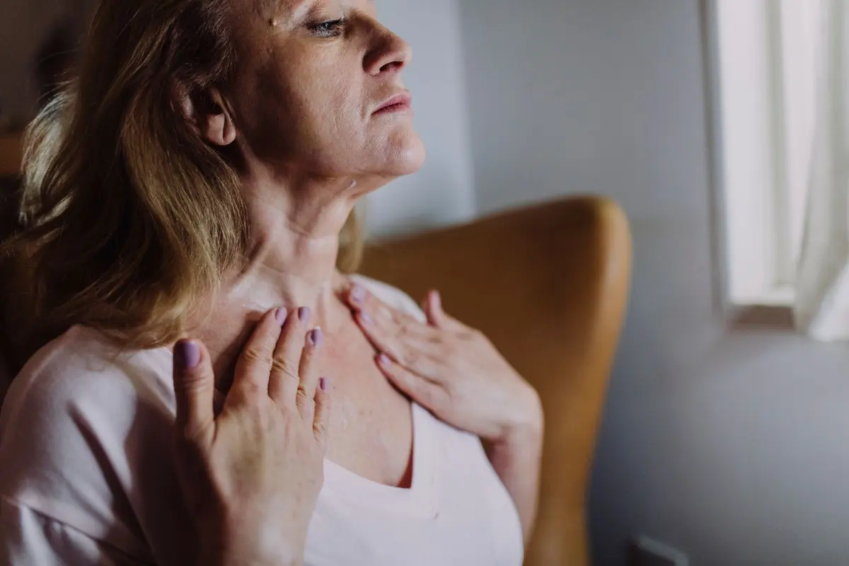 Woman over 50 with shoulder-length hair gently smoothing moisturizer over her neck and collarbone