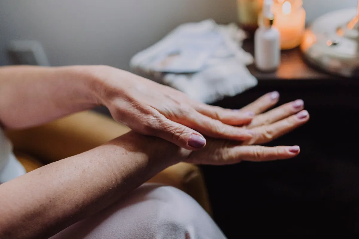 Woman over 50 gently rubbing moisturizer into the backs of her hands, with softly painted nails