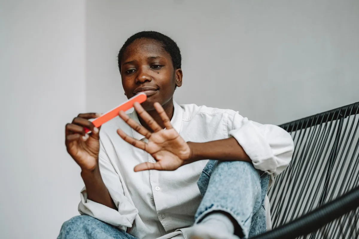 Smiling woman sitting in a chair shaping a fingernail with an orange nail file