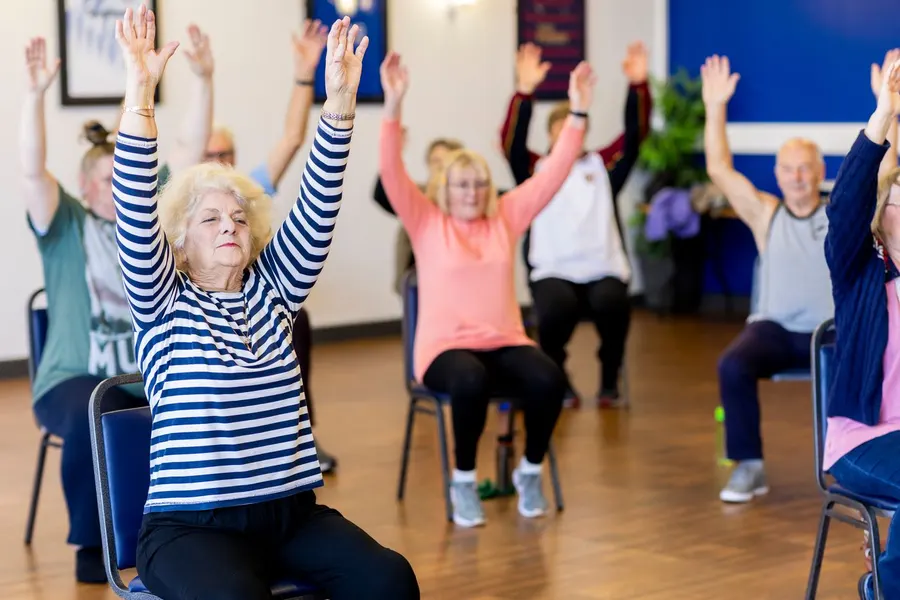 Group of older adults doing a seated stretching class with arms raised