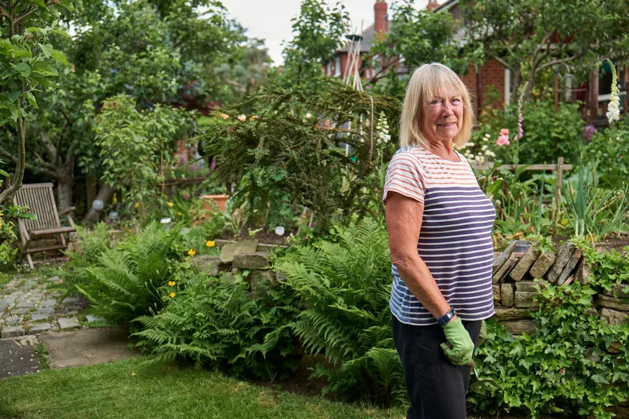 Smiling woman in her sixties standing in her garden holding a hand fork