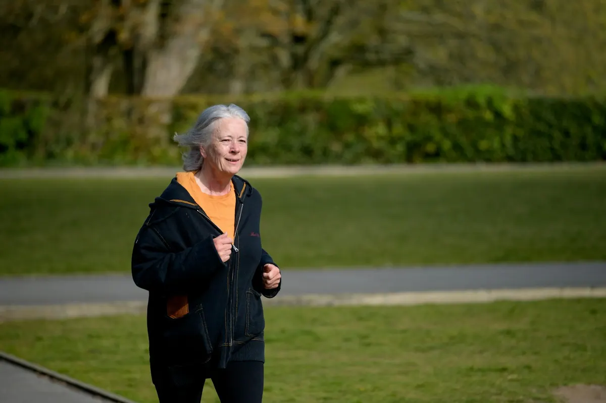 Woman in her sixties with gray hair jogging along a path in a green park