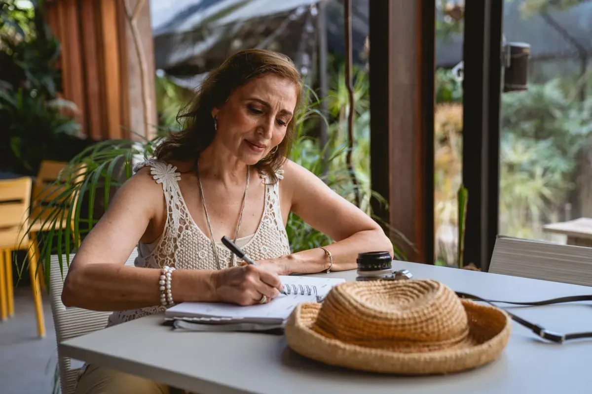 Woman in her fifties writing in a notebook at a cafe table, focused on her notes