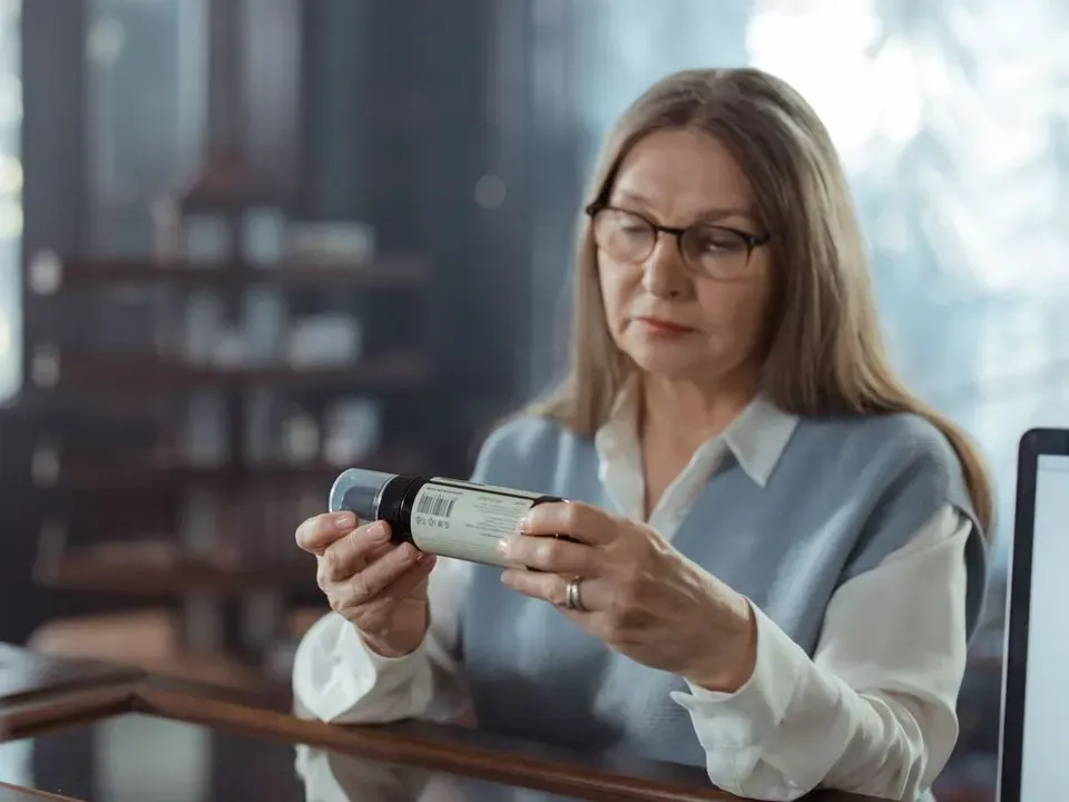 Woman in her 50s wearing glasses and reading the label on a supplement bottle