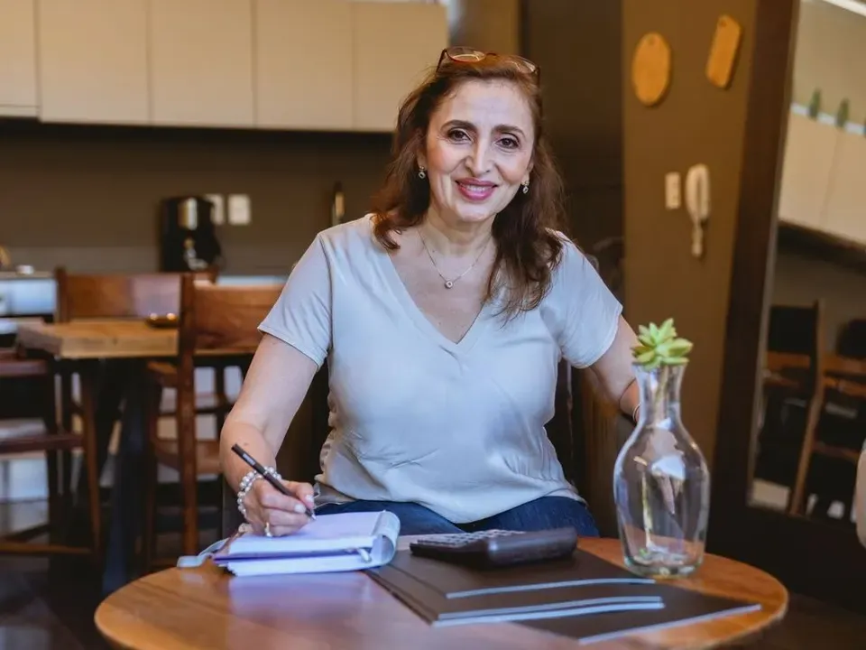 Smiling woman in her 50s writing notes at a table at home