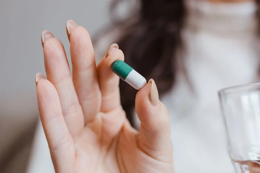 Hand holding a single capsule next to a glass of water