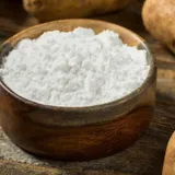 Bowl of potato resistant starch powder next to whole potatoes