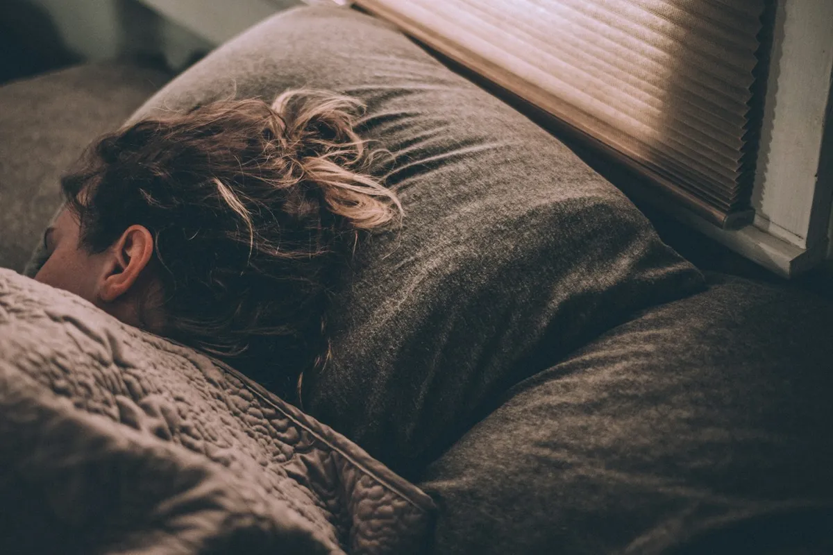 Woman sleeping peacefully under soft gray blankets in the morning light